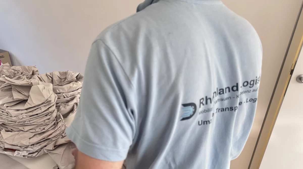 Rheinland-Logistik-Mitarbeiter neben in Papier eingeschlagenem Geschirr