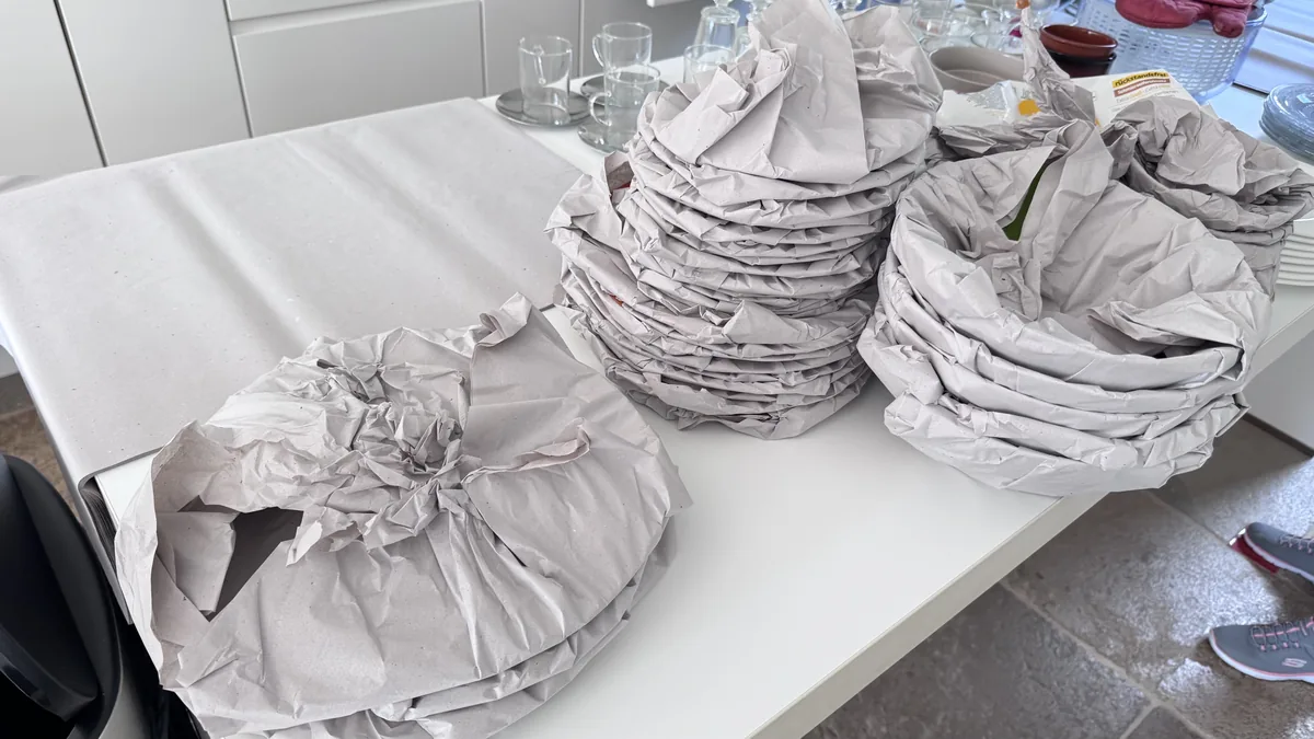 Einzeln in Packpapier eingeschlagene Teller auf einer Arbeitsfläche